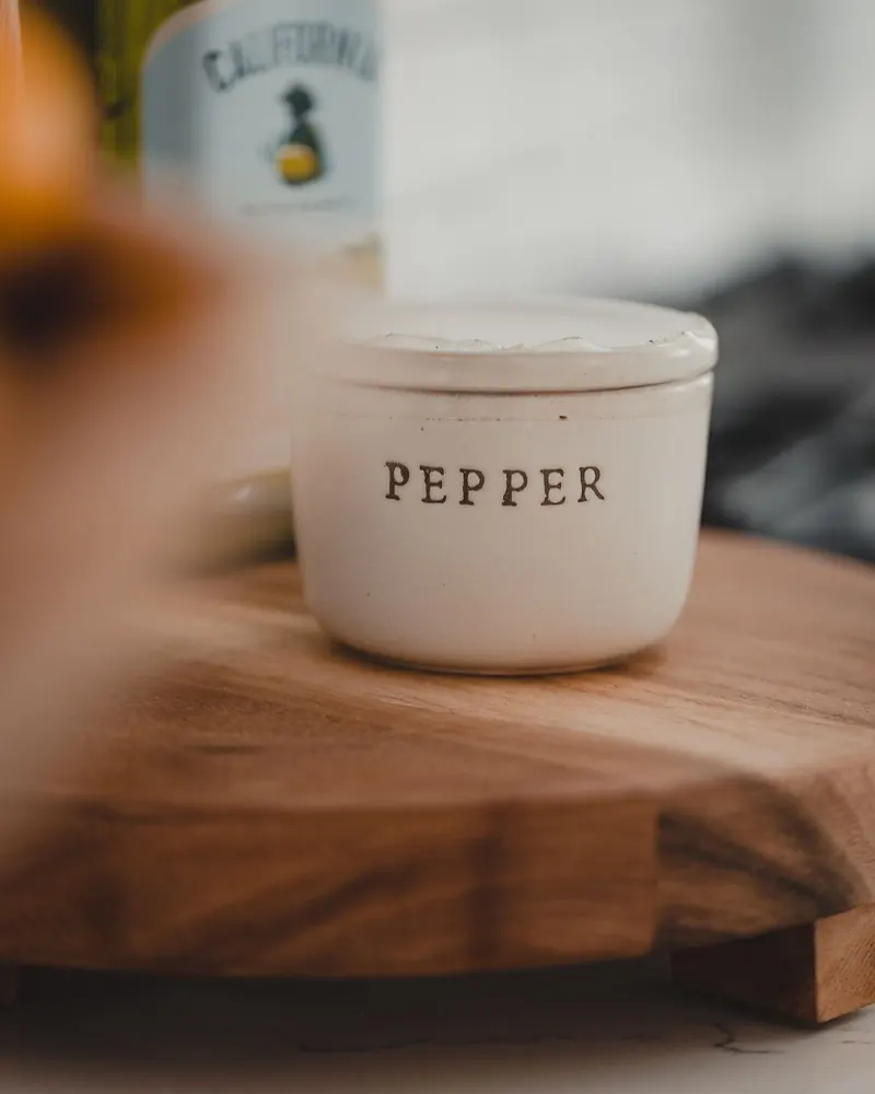 Ceramic pepper jar on a wooden tray with a wine bottle in the background