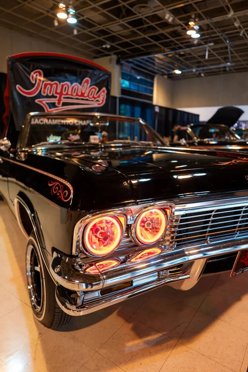 Black-and-white lowrider Chevrolet Impala with glowing red halo headlights at an indoor car show