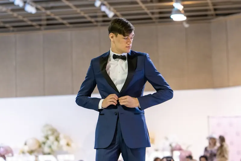 Groom adjusting his blue tuxedo jacket on the runway